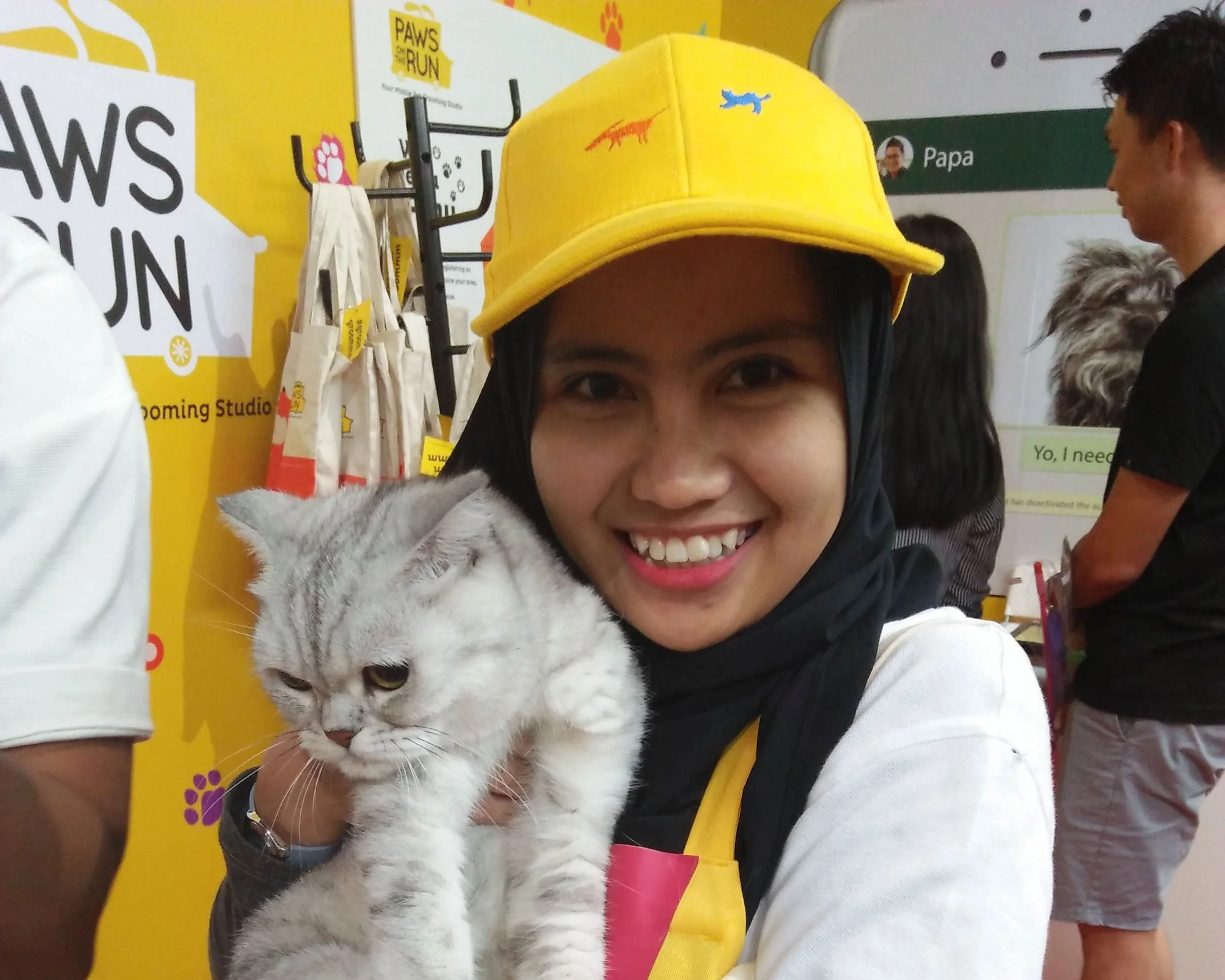 Paws On The Run — a person in a yellow cap holding a fluffy cat at an event booth
